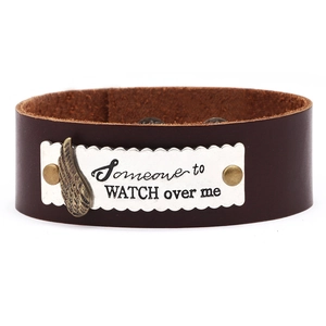 Détail d'un bracelet en cuir marron foncé avec plaque en argent et breloque plume