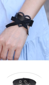 Détail d'un bracelet en cuir noir avec cœur orné, nœud et fermeture à boutons-pression