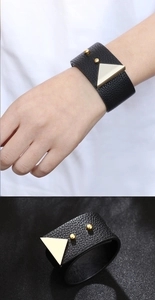 Macro detail of wide black faux leather bracelet with gold triangular metal buckle and studs