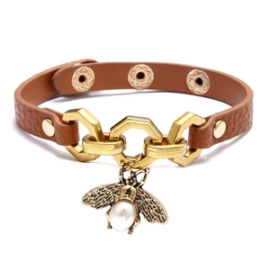 Dettaglio macro del bracciale in pelle marrone con ciondolo a ape dorata e anelli uniti