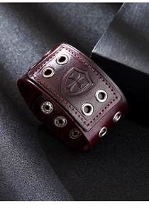 Close-up of wide leather bracelet with embossed cross shield and metal grommet details
