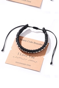 Detail of Morse Code bracelet showing black braided cord and silver beads on a card