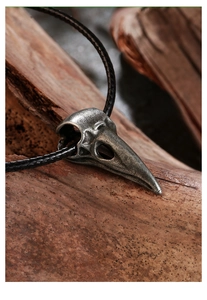 Detail of gothic raven skull pendant with aged metal texture on rustic wood background