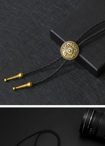 Macro detail of bronze floral engraved Bolo tie slide and black braided leather cord