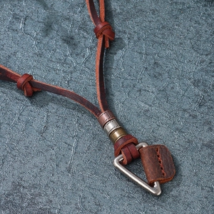 Vintage leather cord necklace with metallic rings and triangular pendant on a stone background