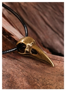 Macro shot of a bronze raven skull pendant with a woven rope on a rustic wood background