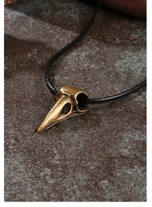 Close-up of bronze crow skull pendant with detailed gothic texture on a stone background
