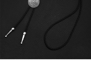 Detail of vintage silver bolo tie with western floral engraving and black braided leather