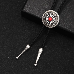 Vintage silver bolo tie with red stone center and black woven cord on textured surface