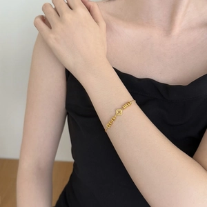 Detail of gold clover bracelet with hollow design and small beads on woman's wrist