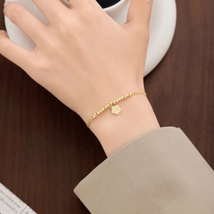 Close-up of golden beaded chain bracelet with delicate floral pendant worn on wrist