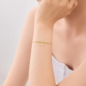 Macro detail of gold flower pendant on delicate beaded bracelet worn on woman's wrist
