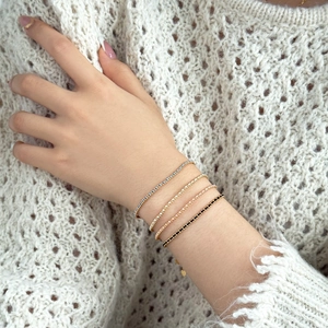 Close-up of four layered tennis bracelets with colorful stones and a small heart charm