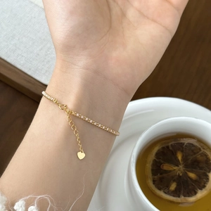 Detailed shot of gold tennis bracelet with pink zircon stones and a heart charm on a wrist