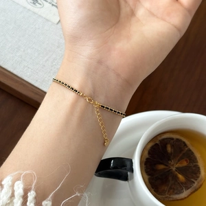 Delicate gold chain bracelet with black beads and heart charm on a woman's wrist