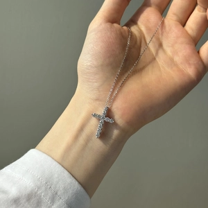 Gros plan du collier croix en argent S925 avec moissanites serties tenu en main