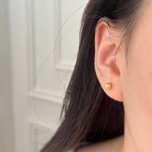 Gros plan d'une puce d'oreille boule dorée minimaliste avec une finition polie brillante