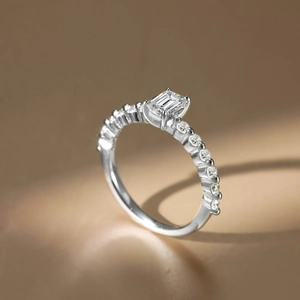 Detailed view of an emerald cut solitaire ring with pave diamonds on a silver band