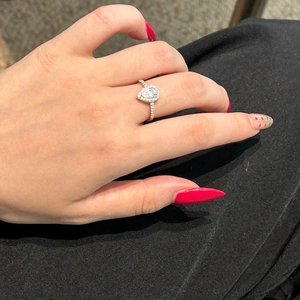 Close-up of a pear-shaped moissanite ring with a halo setting on a finger