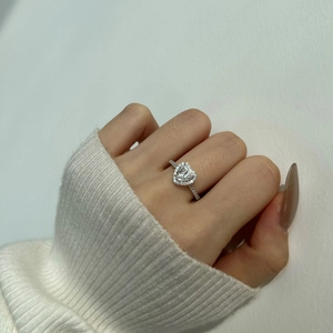 Gros plan d'une bague moissanite en forme de cœur avec serti halo au doigt