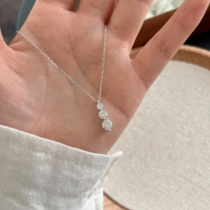 Hand holding S925 sterling silver necklace with three graduated round moissanite stones