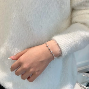 Detail of silver S925 floral bracelet with sparkling zircon stones on a soft white sweater