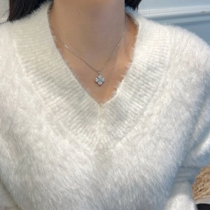 Vue détaillée d'un collier trèfle à quatre feuilles scintillant sur un pull blanc