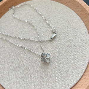 Collier trèfle en argent S925 avec nacre grise présenté sur un support en lin