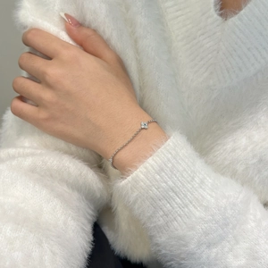 Detailed close-up of a silver clover bracelet with sparkling stones on a white sweater