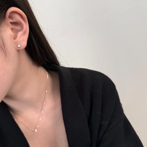 Close-up of minimalist S925 sterling silver solitaire stud earrings and necklace on a model