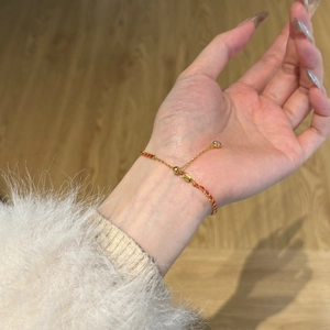Détail du bracelet en cordon rouge tressé avec perles dorées et fermoir réglable