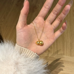 Close-up of a gold wulu pendant necklace with a pearl detail held in a hand