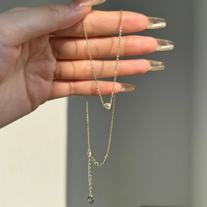 Detailed view of a gold dainty necklace with a round solitaire pendant and heart charm