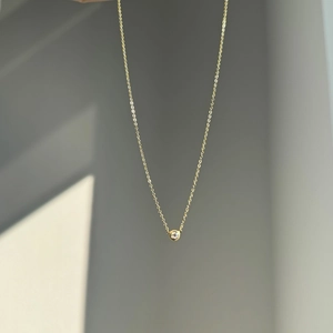 Detail of a minimalist gold bezel-set round pendant necklace on a geometric background