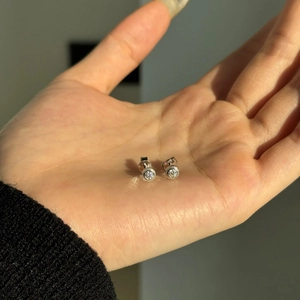 Detail view of S925 sterling silver minimalist round stud earrings held in palm for size