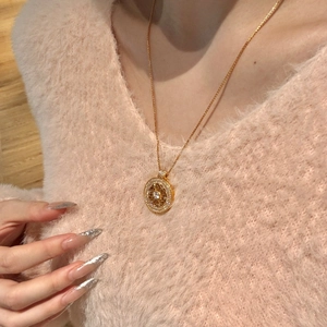Gros plan d'un collier pendentif soleil doré sur un pull en maille rose tendre