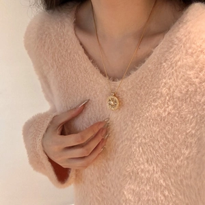 Détail d'un collier pendentif pièce dorée porté sur un pull rose élégant