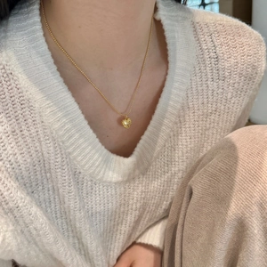 Detail of a textured golden heart pendant on a bead chain worn with a white sweater