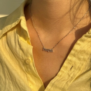 Detalle del collar MAMA de plata con circón en modelo con camisa de lino amarillo