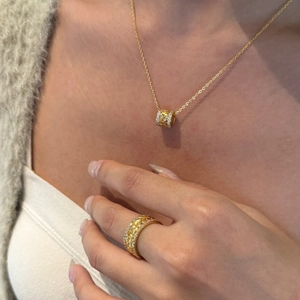 Détail d'un pendentif cylindre doré et d'une bague feuille scintillante sur mannequin