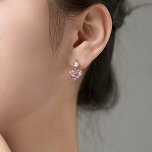 Close-up of heart-shaped pink stone earrings with round diamond accents on a model