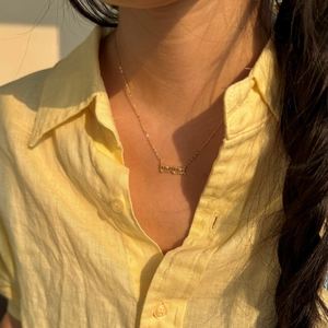 Primer plano del collar con colgante MAMA dorado en mujer con camisa de lino
