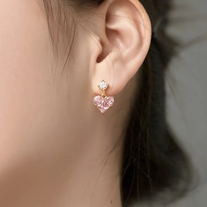 Close-up of dangling gold earrings featuring round clear and pink heart-shaped zircons