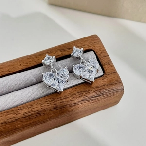 Close-up of S925 sterling silver heart earrings with sparkling crystals on walnut stand