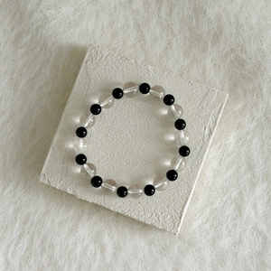 Detailed close-up of black onyx and white crystal beaded bracelet on a white textured stone