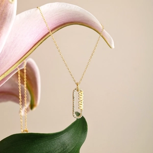 Vue macro du collier MAMA doré avec pierres de zircon suspendu sur des lys roses