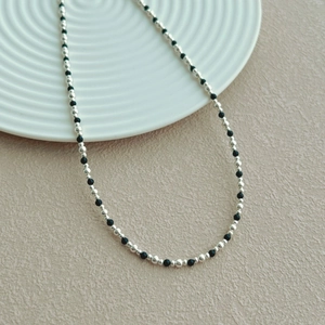 Minimalist S925 silver and black beaded necklace shown on elegant ceramic plate
