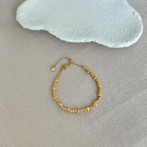 Détail du bracelet à perles dorées avec texture brossée et breloque en zircone