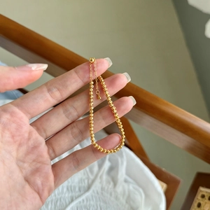 Détail macro d'un bracelet à perles dorées en argent S925 tenu entre les doigts