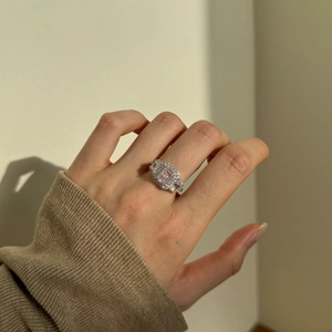 Close-up of a pink cushion-cut silver ring with halo design on a model's finger